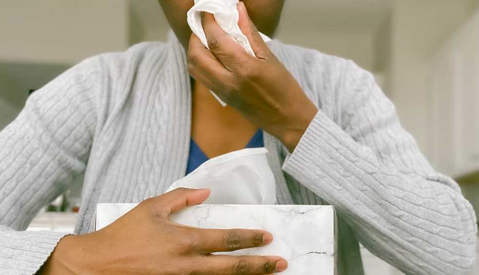 person holding tissue box as she blows her nose