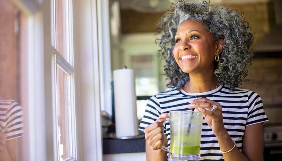 woman drinks a green smoothie as she looks out the window