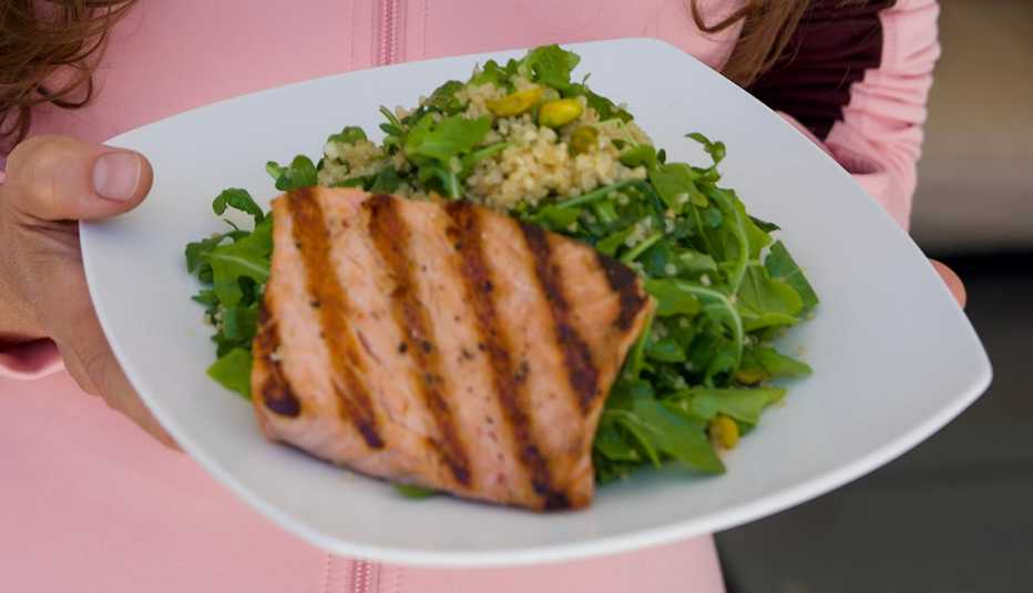 devin alexander holding a dish with her grilled salmon with pistachio and quinoa recipe