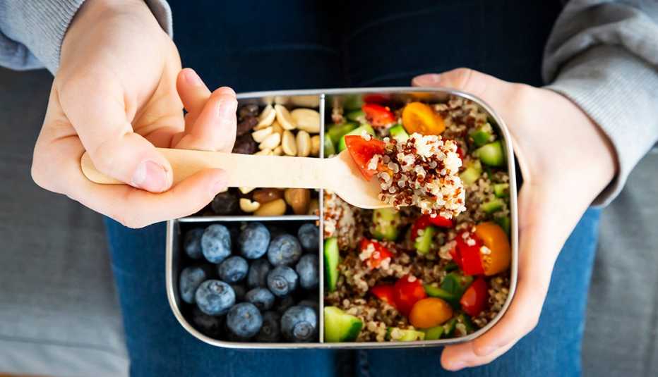bento box with quinoa veggy salad in main compartment and some nuts and blueberries in two smaller compartments