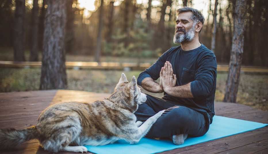 man meditating outdoors on a yoga mat with his dog next to him