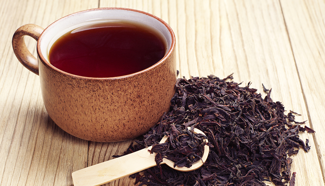 black tea in a cup and dried leaves on wooden background