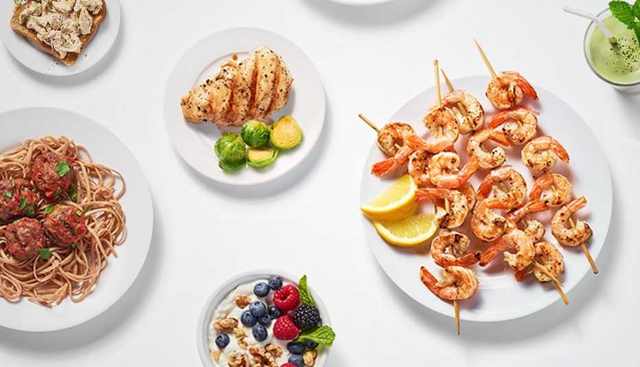 overhead shot of plates of high protein healthy foods shrimp skewers smoothie tuna on toast chicken breast and greek yogurt