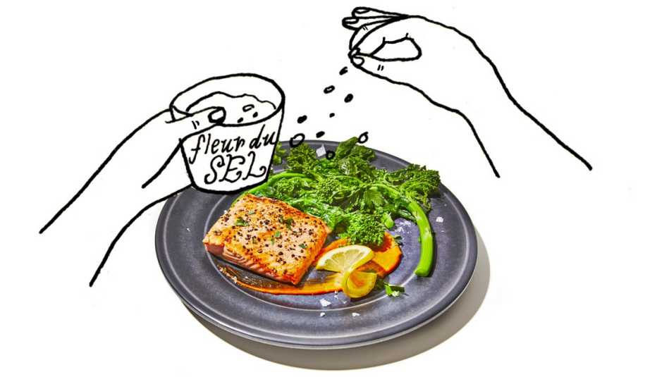 plate of salmon and broccoli with hands sprinkling fleur du sel on it