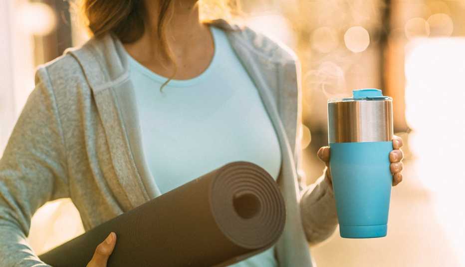 Healthy fit young woman headed to yoga with yoga mat and coffee cup