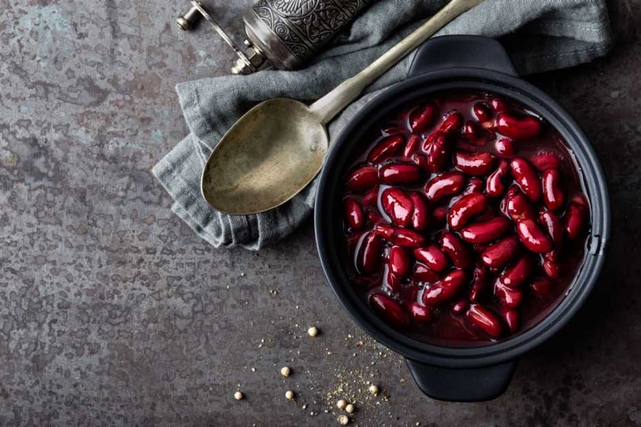 a bowl of boiled red kidney beans rests on a dish cloth with a cooking spoon