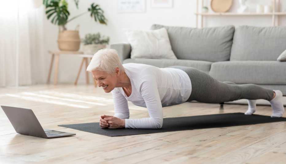 woman in plank position on a black yoga mat during an at-home online pilates class