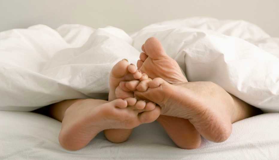 two pairs of feet in a bed underneath a blanket