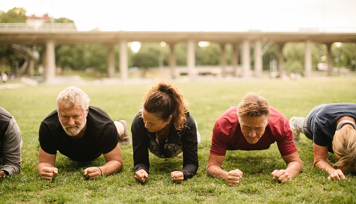 group of middle aged people all doing plank exercise outdoors in a park