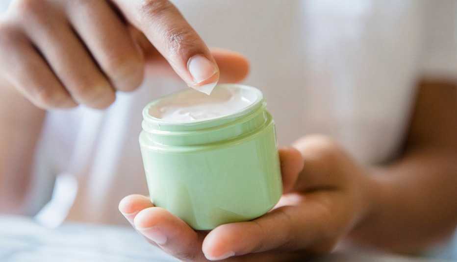 A closeup of a woman dipping her finger in jar of moisturizer