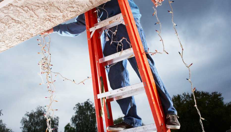 a man on a ladder hangs holiday lights on a roof