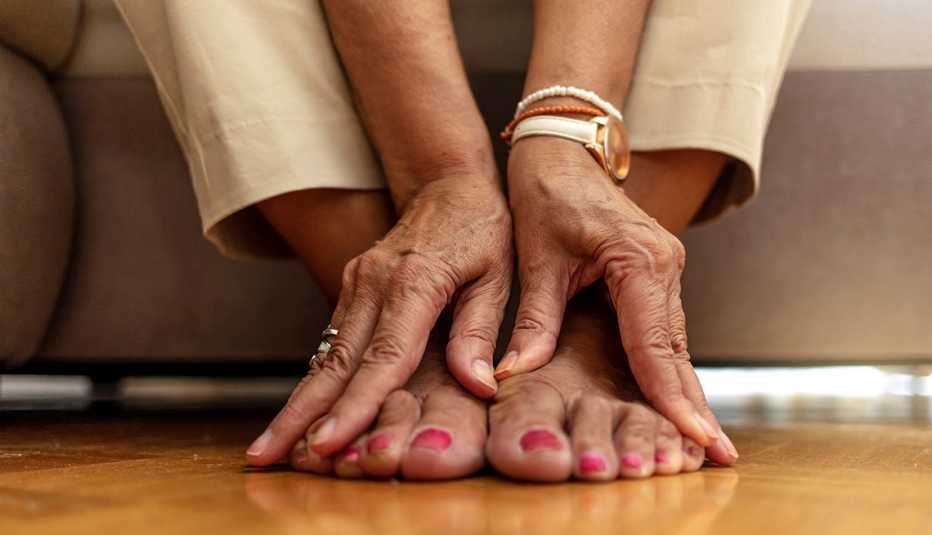 close up of a woman's hands massaging her feet and toes on a hardwood floor