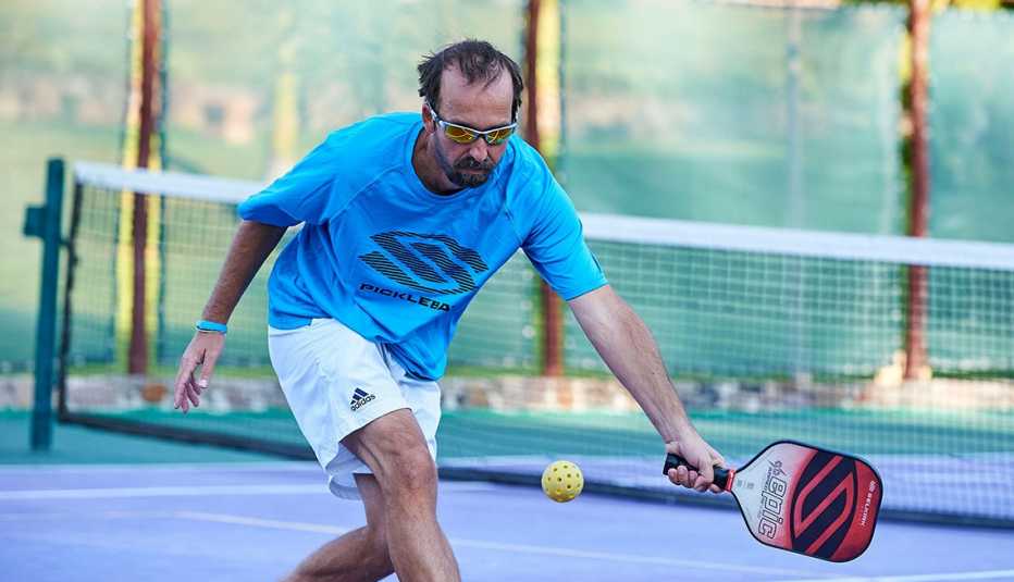 a man in a blue shirt and white shorts  aging gracefully playing pickleball prepares to hit the ball back to an unseen player on the court