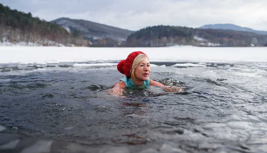 woman wearing a winter hat swimming outdoors in an icy lake or river in winter with snow surrounding the water she is submerged up to her neck