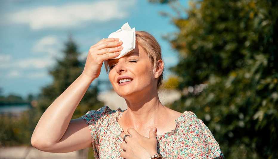 sweaty woman outside in hot weather, holding a tissue to her forehead