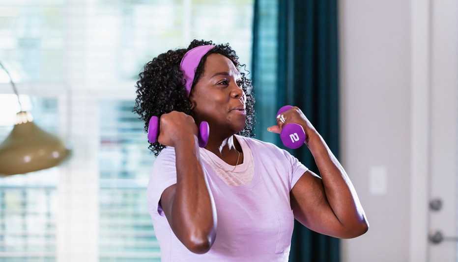 a woman in a purple shirt and headband lifts matching purple two-pound dumbbells in her living room