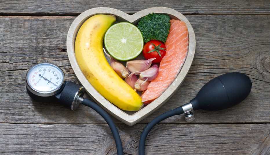 an aneroid blood pressure cuff frames a heart-shaped basket filled with produce and salmon