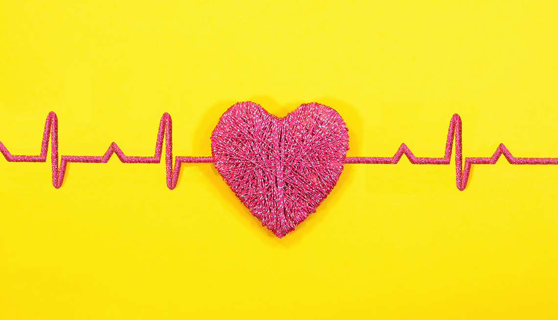 a red heart made of yarn shows a heart beat reading of a normal heart rate on a bright yellow background