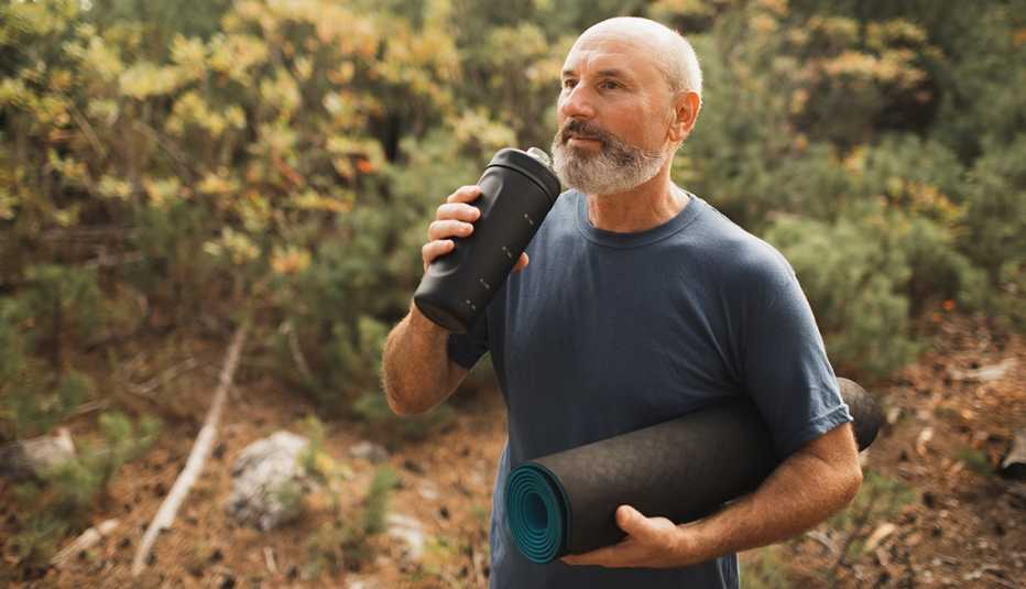 man drinking water outdoors and holding yoga mat