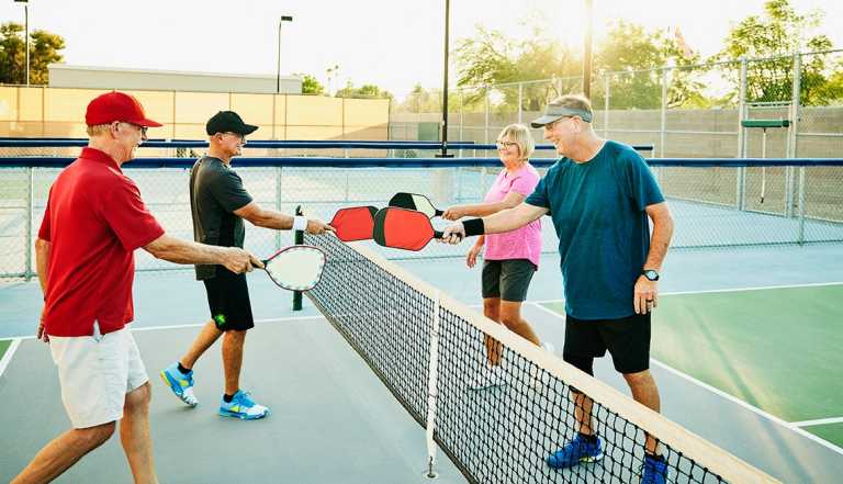 four people meet at the net on a pickleball court and touch paddles