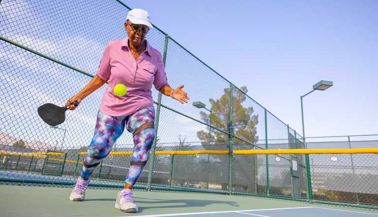 woman serving a pickleball on a court