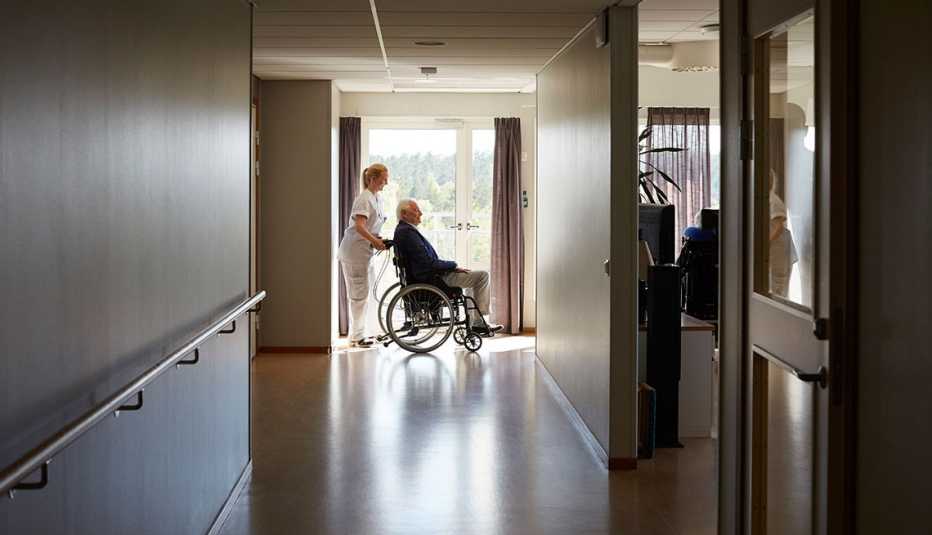 nurse pushing an older man on a wheel chair at a nursing home 