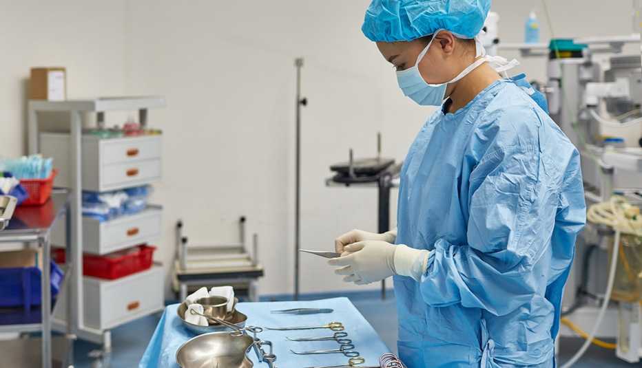 A side view of a female surgeon arranging medical tools on table. Healthcare worker is preparing for surgery. She is wearing scrubs in operating room at hospital