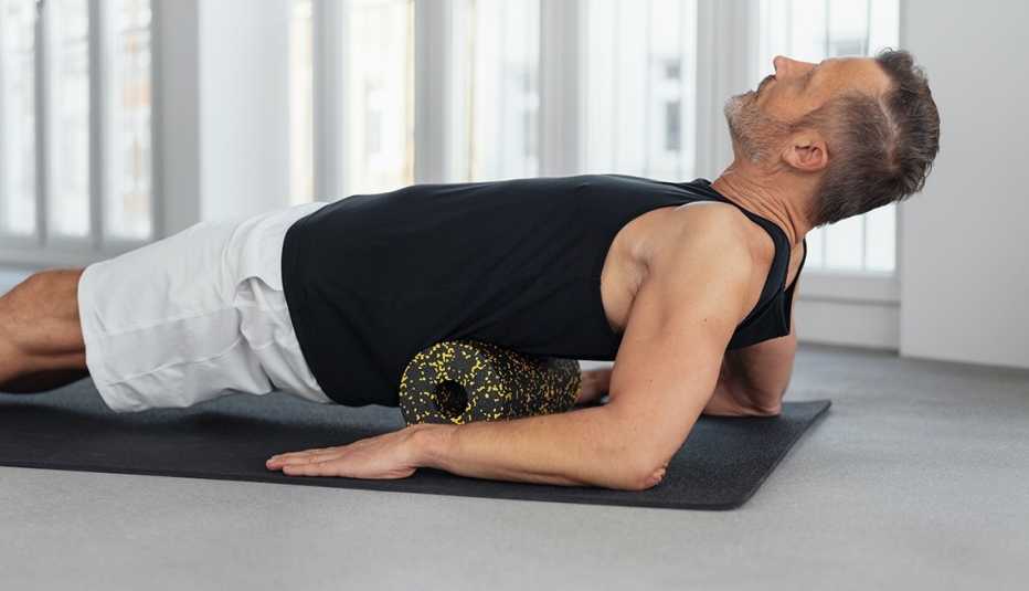 Man using a foam roller to massage his back and spine on a gym mat on the floor