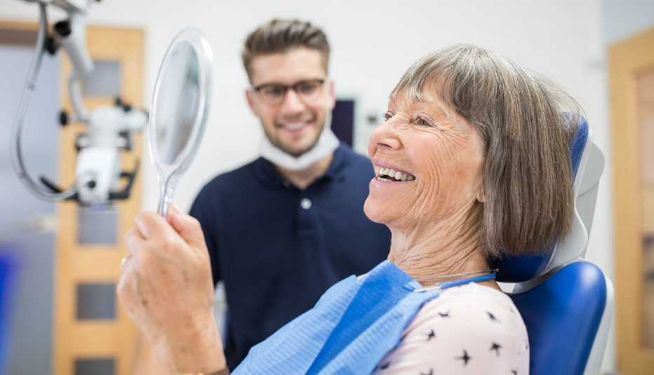 patient checking her teeth into a hand mirror after her dental treatment. Senior patient checking her teeth after treatment at dentist