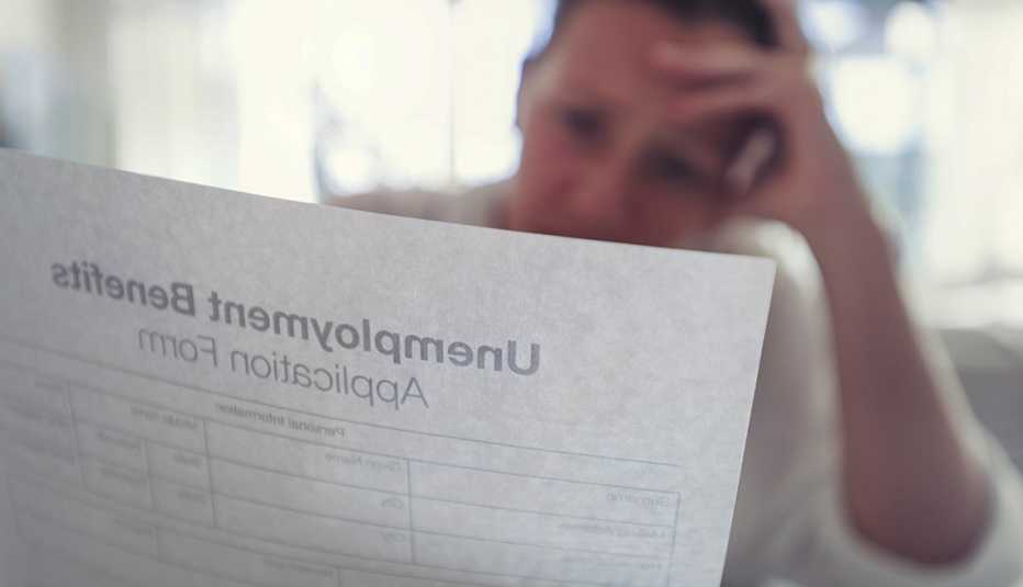 stressed figure in soft focus sits behind a semi-transparent sheet of paper that appears to be an unemployment benefits application form