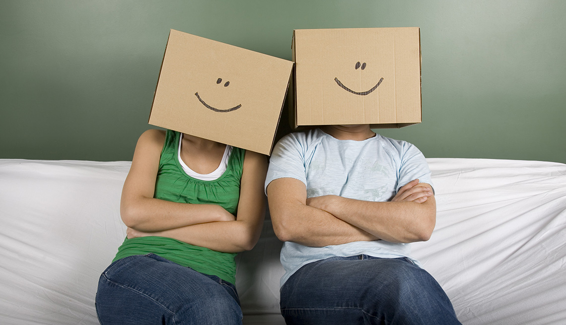 Couple Sit On Sofa Covered In White Sheet With Boxes Covering Their Faces With Smiley Faces Drawn On Them, AARP Home And Family, Can Moving Really Make You Happier? 