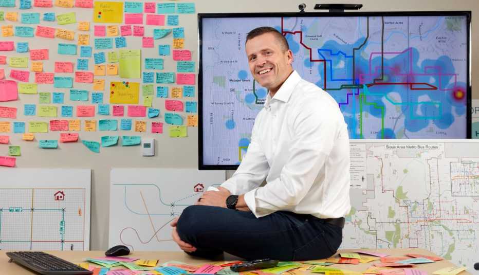 paul tenhaken the mayor of sioux falls south dakota sits on the desk in his planning office where the walls are covered in colorful post it notes and maps