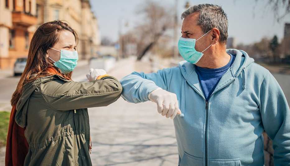 Man and woman, two people with protective masks  greeting each other with elbows instead of handshake, alternative non-contact greeting during coronavirus epidemic, standing on the street in safe distance