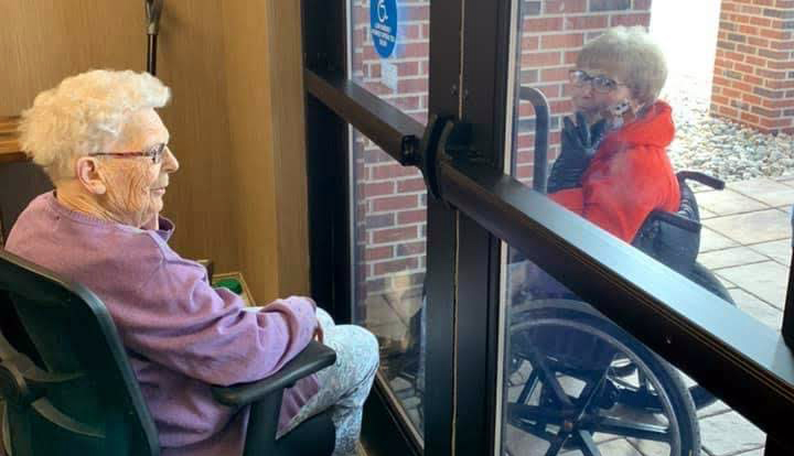 two women interact through the closed glass doors of an assisted living facility r
