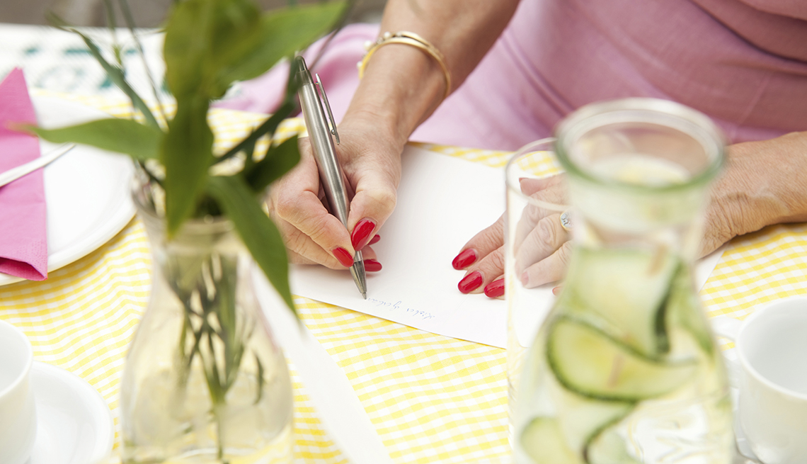 the hands of a woman sitting at a table writing in a sympathy card