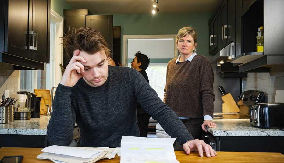 mother watching young man looking over mounting debts at kitchen table
