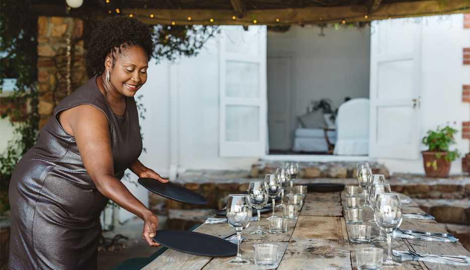 Smiling woman wearing an evening gown setting up a table for a dinner party on her outdoor patio