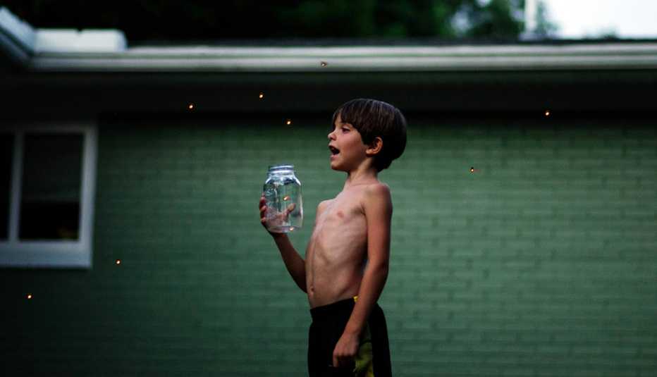 a child with a jar of lightning bugs against an exterior wall