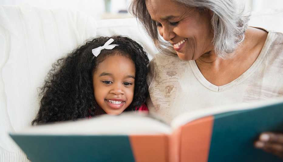 a grandmother and granddaughter sit together reading an orange and green book