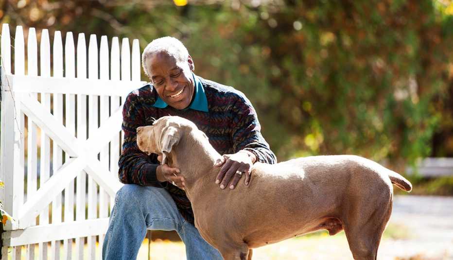 a smiling man pets a brown dog outside next to a white fence