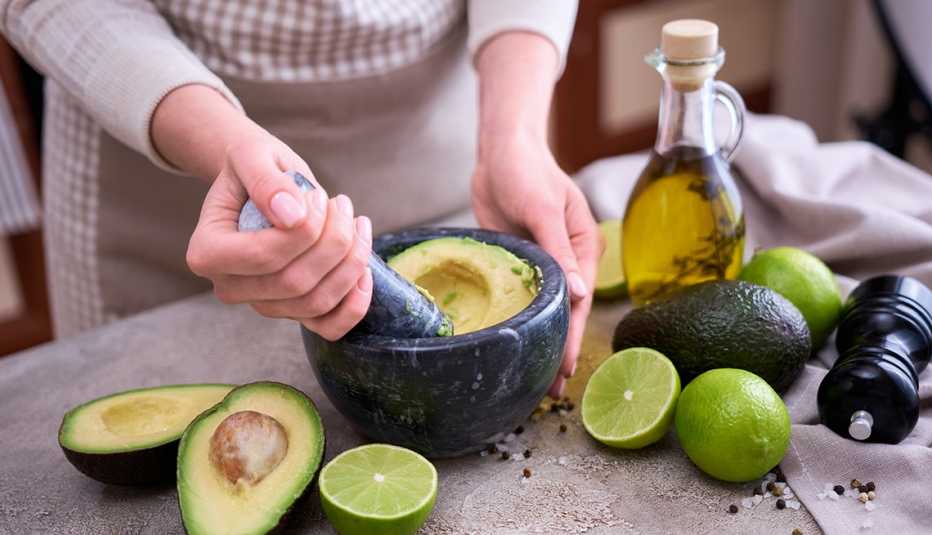 close up of a woman making guacamole with avocados and a bottle of olive oil and a jar of pepper to reap the health benefits of healthy fats that won't make you gain weight