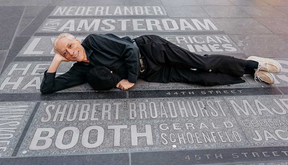Wish of a Lifetime recipient Howard Shapiro poses reclining on sidewalk in Times Square that features the names of Broadway theaters.