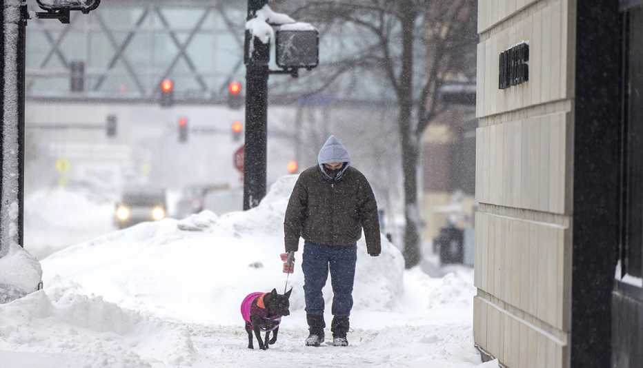 a man walks his dog along the sidewalk during a snowstorm in Iowa