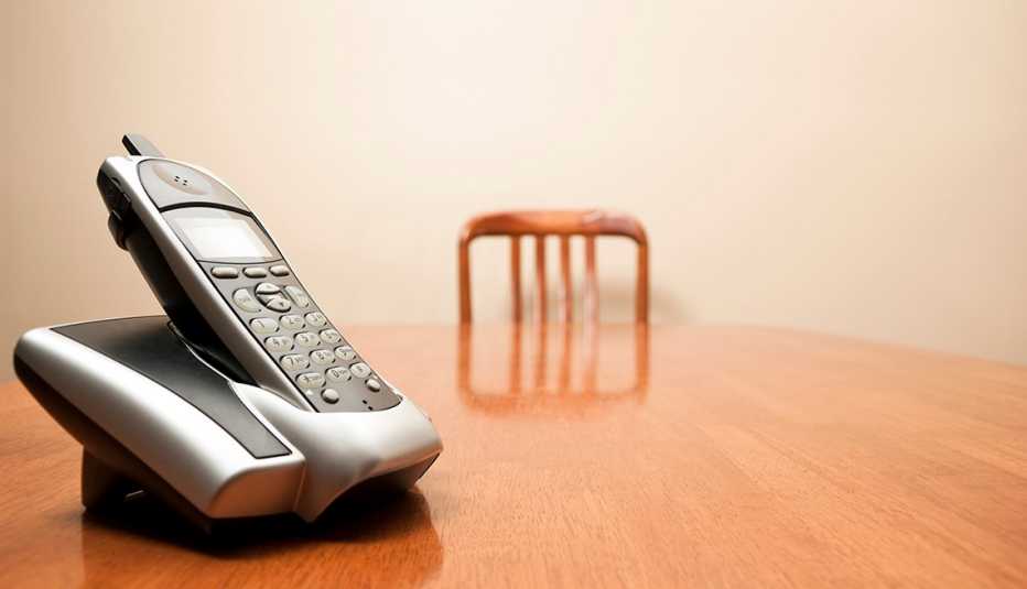A modern cordless phone sits on an empty table. Focus on phone in foreground. 