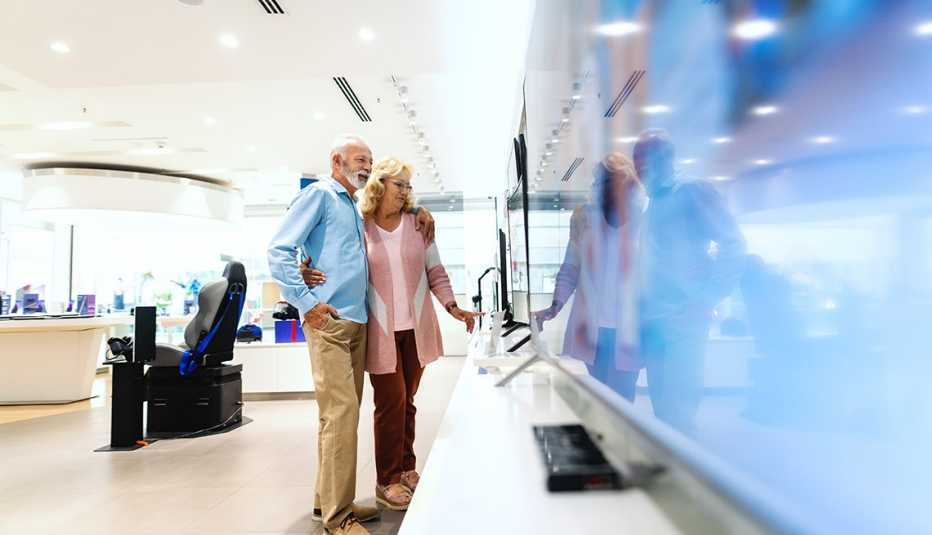 Happy old married couple hugging and looking for new plasma tv to buy. Tech store interior.