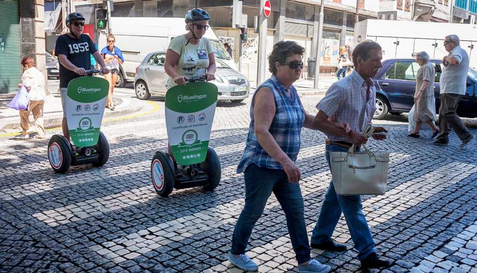 Two pedestrians cross the cobbled Rua Sa da Bandeira, followed closely by a pair of Segway riding tourists.
