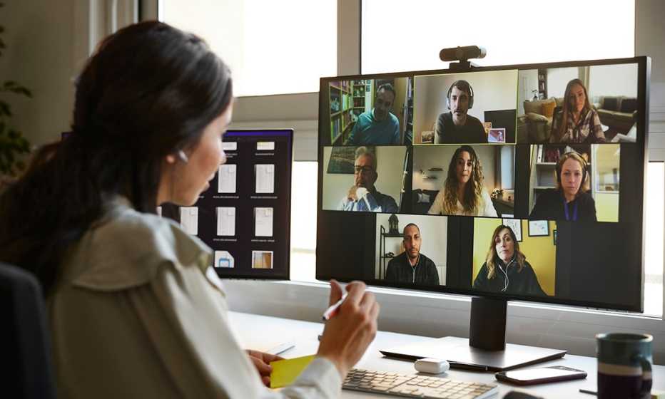 a woman in a white shirt sits at a monitor talking to colleagues remotely
