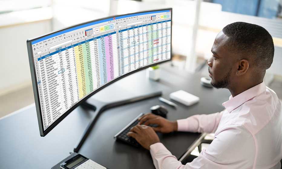 a man in a pink shirt in an office looks at spreadsheets