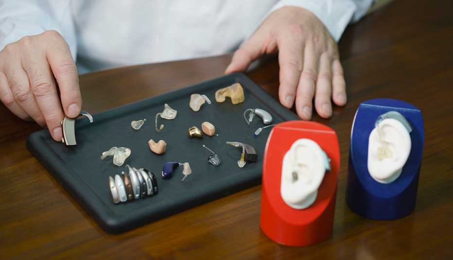 A doctor's hands showing a sample of a hearing aid. Other hearing aids on display.
