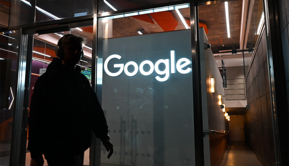 a man walking by in the dark as a google sign glows behind him